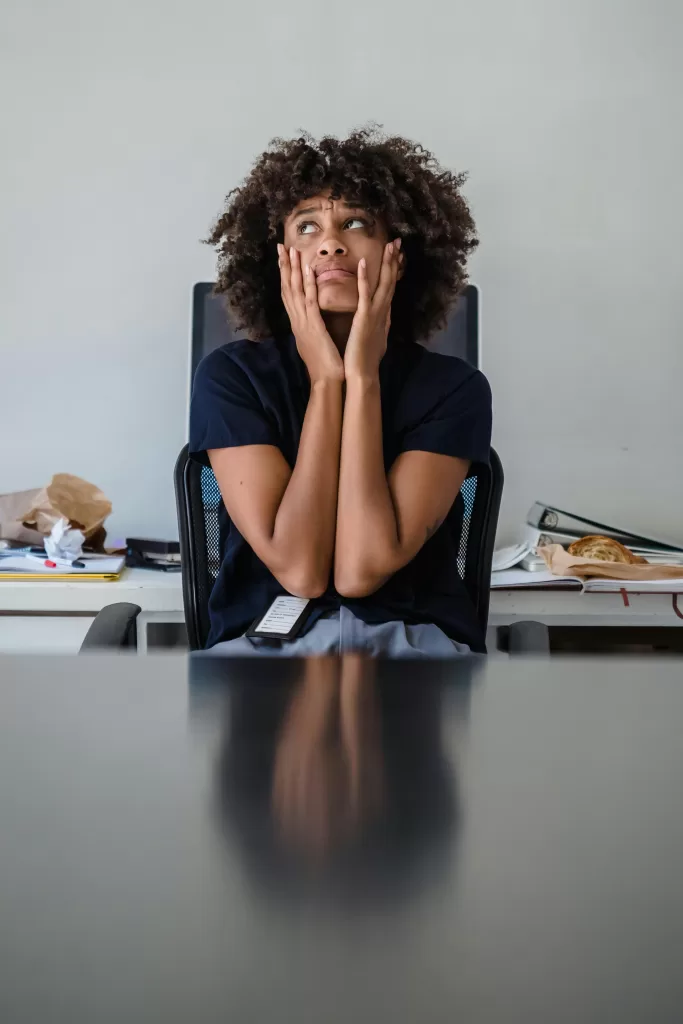 Contemplative woman in office, hands on face, expressing frustration.