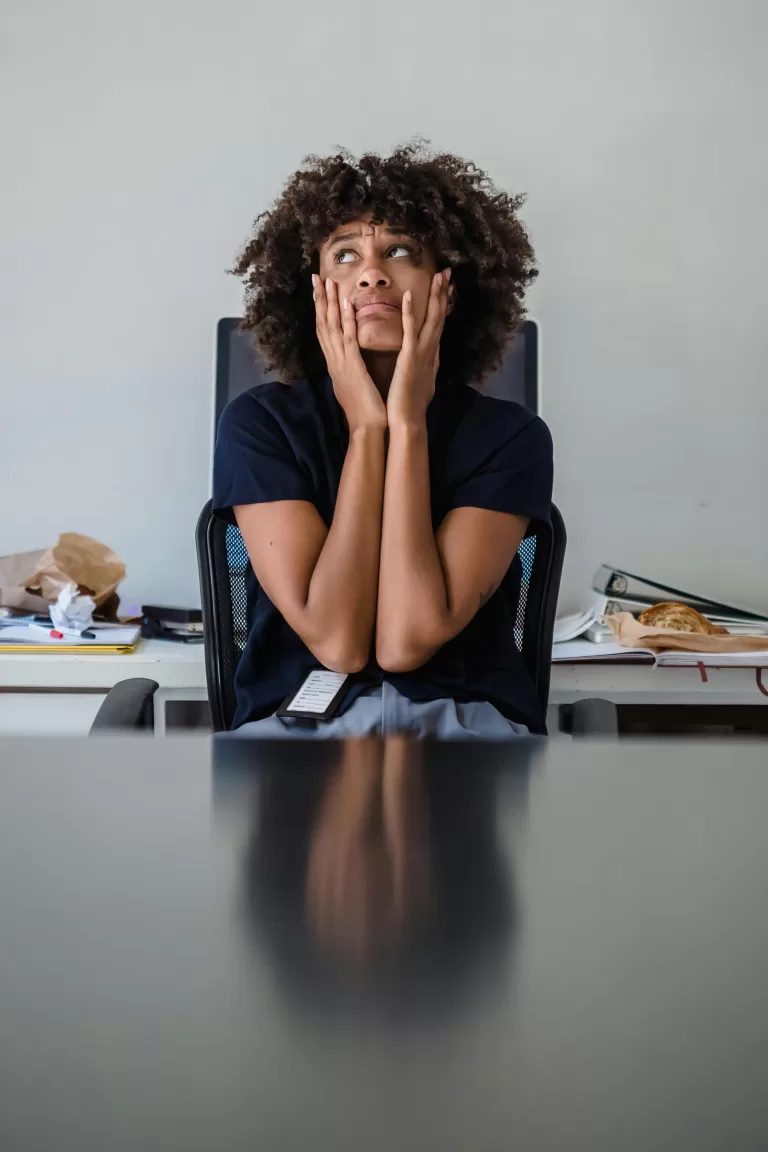 Contemplative woman in office, hands on face, expressing frustration.