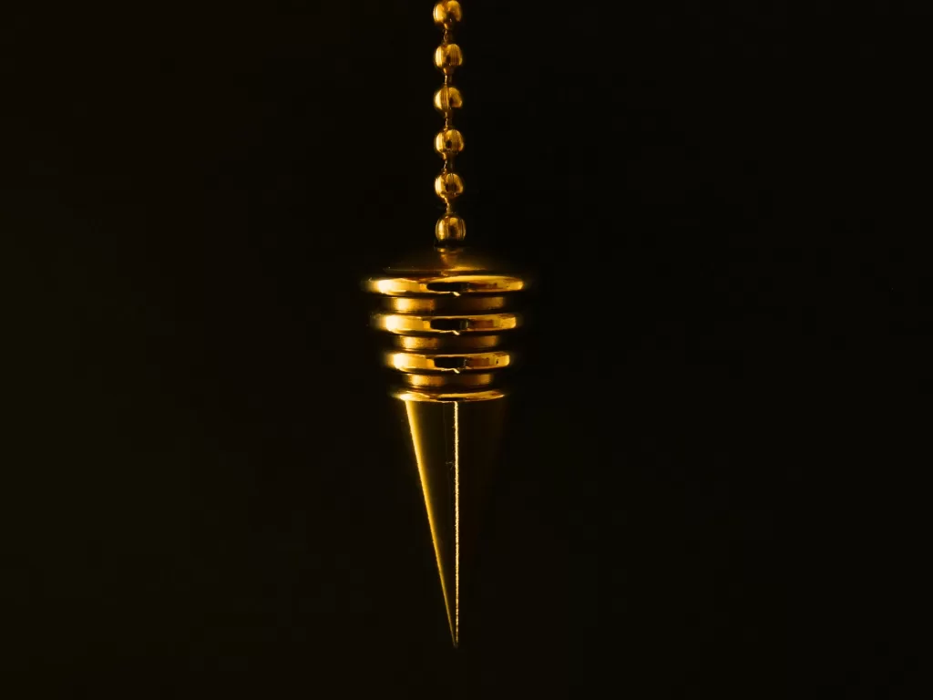 An elegant gold pendulum with chain on a mysterious black background.