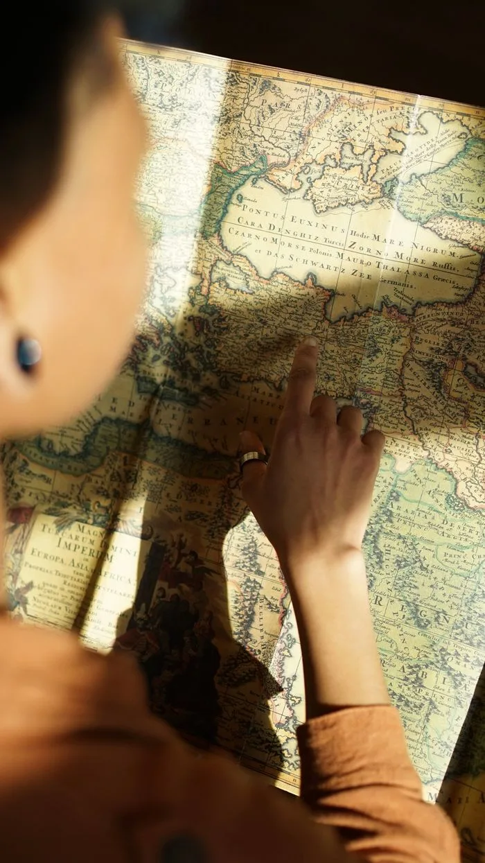 A woman examining an ancient map with her finger pointing, in a sunlit indoor setting.